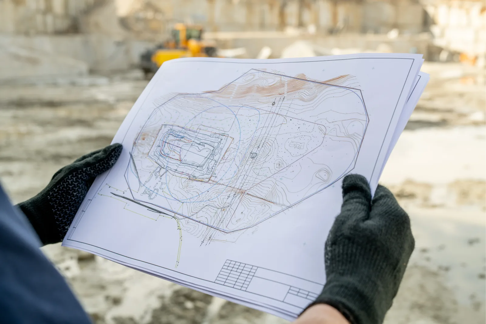 Gloved hands holding a printed site drawing on a construction site